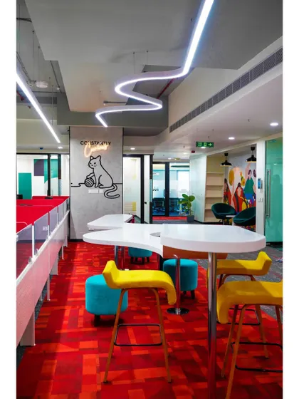 A high-top table setup near the workstations, perfect for quick team huddles. The "Constantly Curious" cat graphic adds a touch of whimsy and reinforces a key company value.