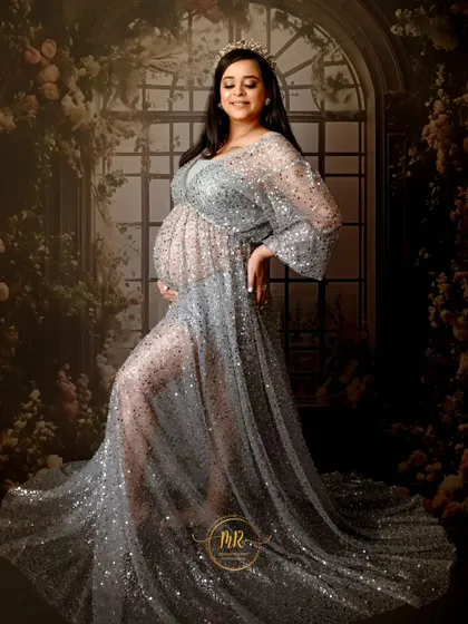 A full-length portrait in a stunning silver sequin gown. The floral archway backdrop adds a touch of romance and elegance to this glamorous maternity photo.