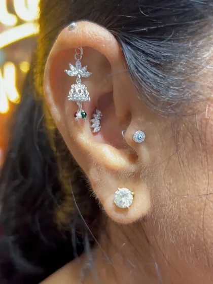 A traditional jhumka-style hanging brings a touch of Indian heritage to this modern ear stack, complemented by an evil eye stud and a solitaire.