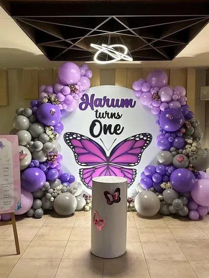 The complete butterfly themed first birthday setup, including the main backdrop, a milestone board on an easel, and decorative baby blocks.