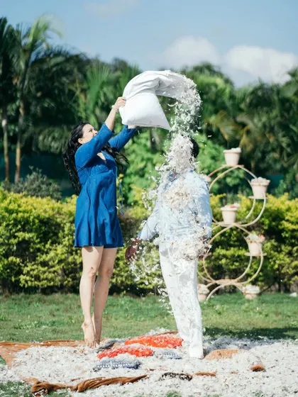 A fun and spontaneous pre-wedding moment as the bride-to-be playfully showers her partner with feathers from a pillow fight in a park.