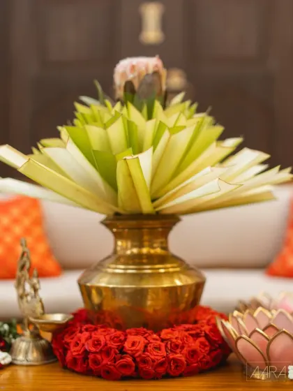 A traditional brass pot (kalash) filled with folded palm leaves and surrounded by red roses. This 'Divya Stambh' detail is a beautiful symbol of divinity and craftsmanship.