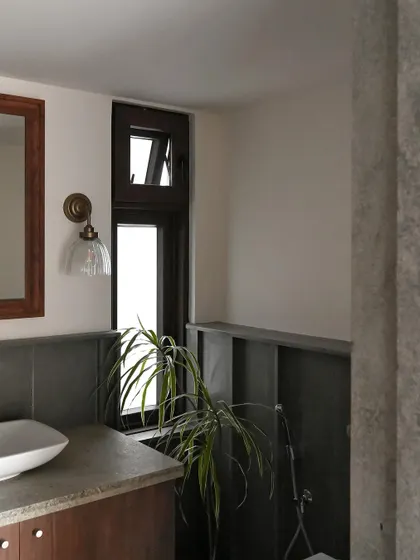 This bathroom combines white walls with a wainscoting of dark Kota stone. A narrow window and a vintage-style wall sconce provide layers of light, while a houseplant adds a touch of life.