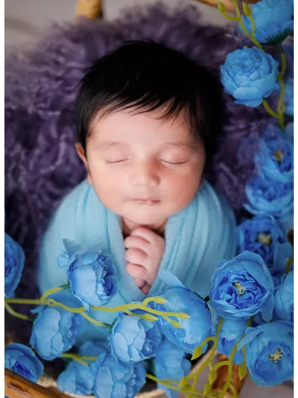 A close-up of a baby boy surrounded by blue flowers in a basket, creating a soft and serene portrait.