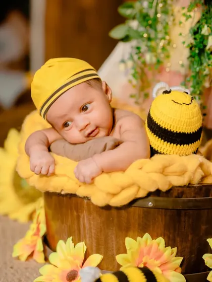 A curious newborn peeking out from a bucket in a bumblebee-themed setup. This shot captures a precious, alert moment.