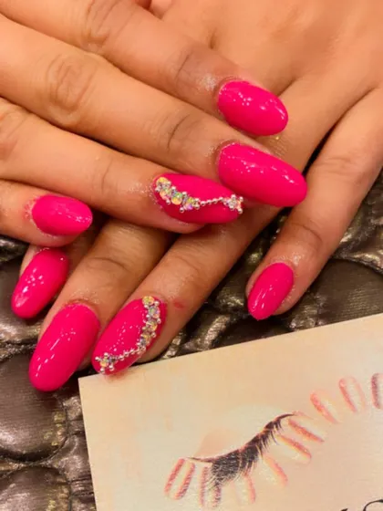 Vibrant pink almond nails perfect for making a statement. The ring fingers are adorned with a beautiful, curved line of iridescent rhinestones.