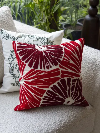 A bold red Christmas cushion with an abstract floral pattern, paired with a white cushion featuring delicate green embroidery. These pieces add a touch of luxury and festive cheer.