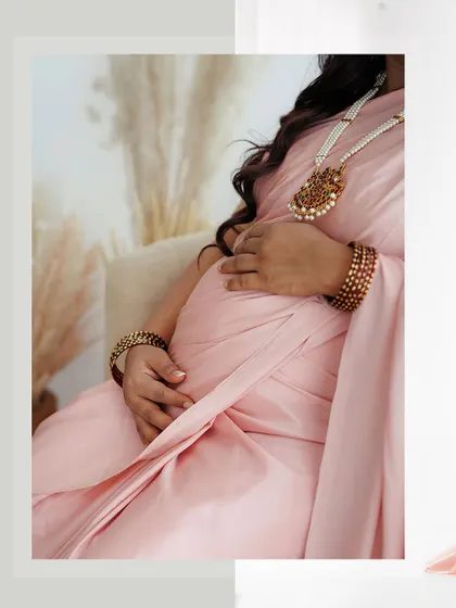 A detail shot focusing on the baby bump and the beautiful texture of the saree. The client's hands, with their simple manicure, gently cradle her belly.