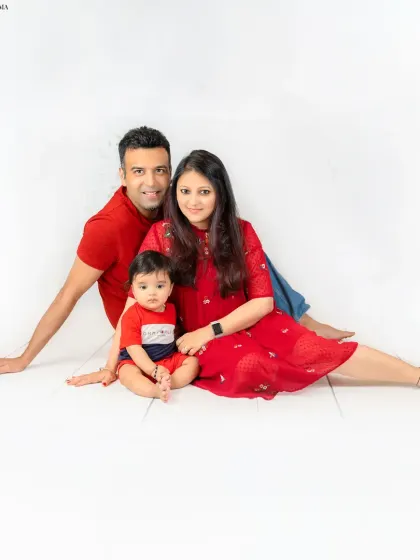 A relaxed family portrait with parents and their baby sitting together on the floor in coordinated red outfits. Their happy expressions make this a heartwarming image.