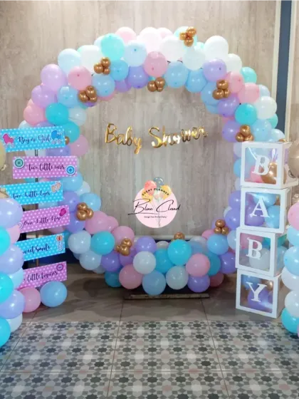 A complete gender reveal party setup with a circular balloon arch, 'BABY' blocks, and themed signposts.