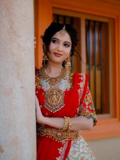 A classic pose, leaning against a pillar. This shot showcases the beautiful embroidery on the blouse and the traditional elegance of the entire bridal ensemble.