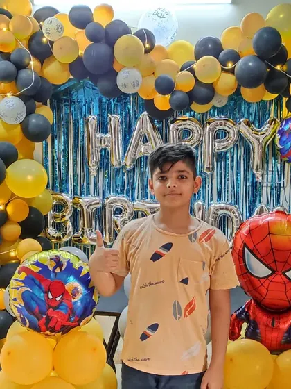A happy birthday boy with his Spiderman-themed decoration. This setup uses a yellow and black color scheme with a blue shimmer curtain, creating a unique look for the popular superhero theme.