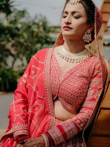 A close-up portrait of the bride in the sun, highlighting the intricate embroidery on her red lehenga.