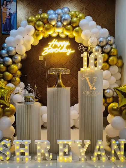 A grand 10th birthday celebration with a gold, silver, and white balloon arch and large marquee letters.