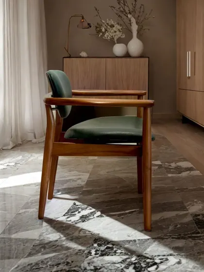 A classic wooden armchair with deep green upholstery, pictured in a beautifully lit, serene setting. This piece embodies timeless design and quality craftsmanship.