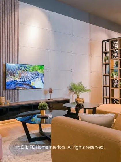 A cozy living room setting with a comfortable sofa, a soft pink armchair, and a textured wall with integrated lighting. The space is defined by its warm and inviting atmosphere.