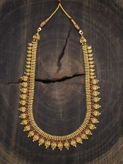 A classic kasu-style haram or long necklace. This piece features a traditional coin design with intricate carvings, set in a rich gold tone with red stone accents for a timeless appeal.