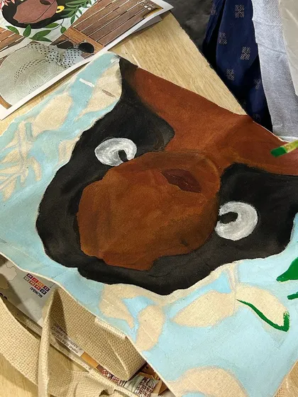 A work in progress. This participant is painting a cute capybara on their tote bag, a fun and whimsical design.