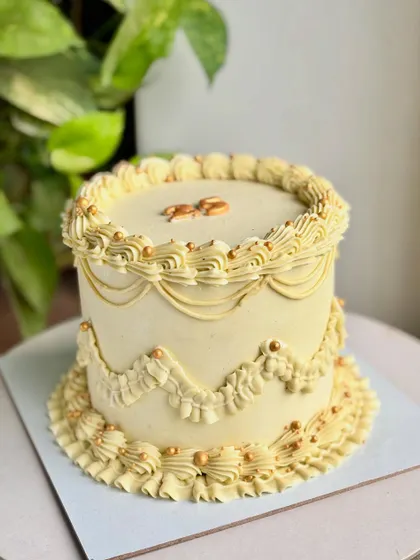 A slightly different angle of the golden vintage cake, showcasing the "25" topper and the beautiful texture of the buttercream piping against a leafy background.