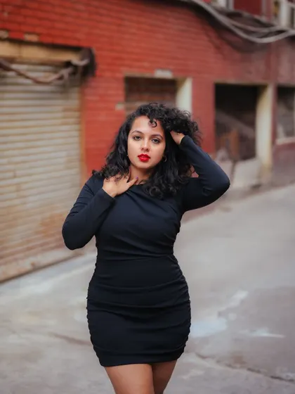 A powerful portrait of a model in a black dress, set against a gritty urban alley. Her pose and the raw background create a moody and expressive shot.