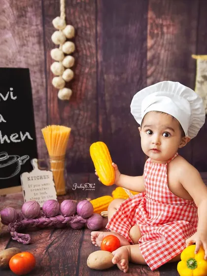 Surrounded by fresh vegetables and pasta, this little chef is exploring all the ingredients. The rustic wooden backdrop completes the kitchen feel.