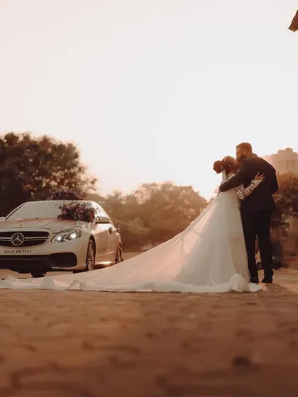 A magical "Just Married" moment, with the couple embracing in front of their wedding car, the bride's long train flowing behind them.