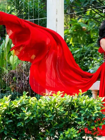 A couple shares an intimate moment in a garden, her flowing red gown adding a vibrant splash of color and drama to the natural surroundings.