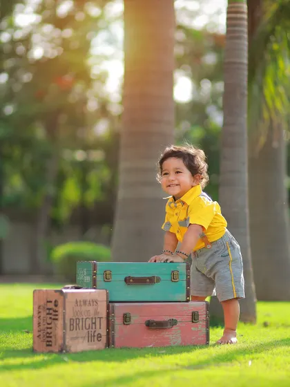 Using vintage props like these colorful trunks adds a touch of charm to outdoor kids' photoshoots. This little boy is all smiles during his sunny park session.