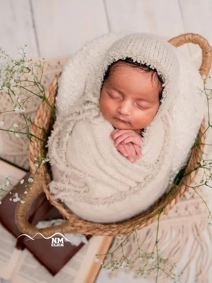 So peaceful and pure. This classic newborn shot features a beautifully swaddled baby in a simple basket, adorned with delicate baby's breath for a timeless look.