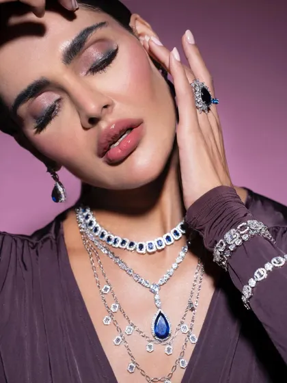 A serene and luxurious portrait showcasing a layered sapphire and diamond necklace set. The styling emphasizes elegance, with closed eyes drawing attention to the makeup and the brilliance of the jewels.