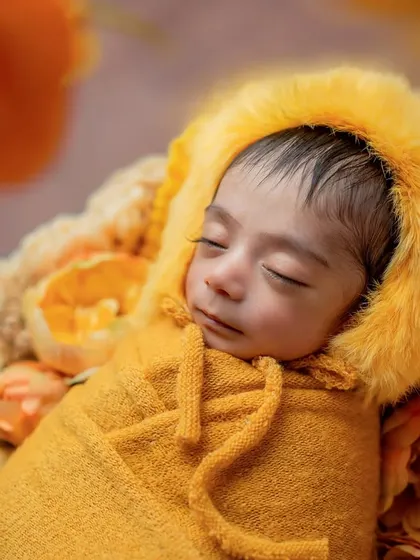 A detailed close-up of the baby's face, highlighting their long eyelashes and the soft texture of the fuzzy yellow bonnet.