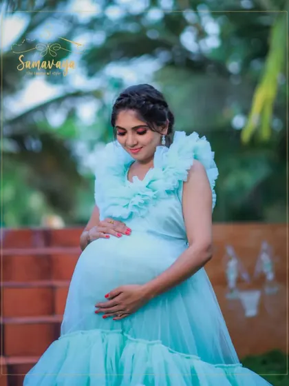 A close-up portrait focusing on the mother's loving gaze towards her bump. The soft frills of the gown frame her face beautifully.
