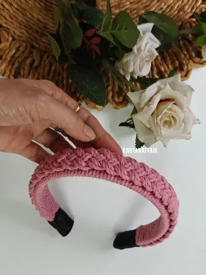 Holding the baby pink braided macrame hairband. This color is perfect for kids or for adding a soft, feminine touch to your look.