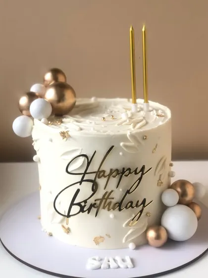 An elegant white and gold birthday cake with a modern script topper and balloon clusters.