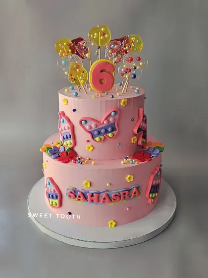 A pop-it themed cake for Sahasra's 6th birthday. This two-tier vanilla and strawberry cake is covered in colorful, edible pop-it designs.