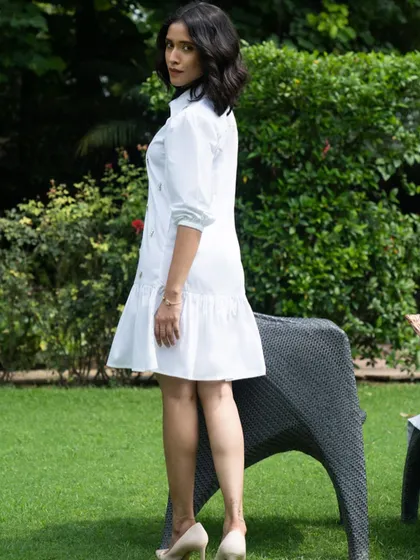 An outdoor campaign shoot for a fashion brand, set in a lush garden. The natural light and green background make the crisp white dress stand out beautifully.