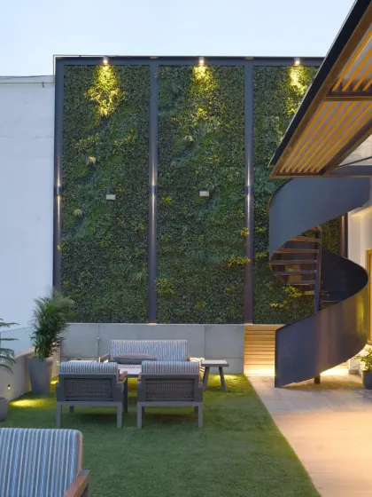 The terrace garden of the Screen House is an inviting retreat with a lush green wall. A striking spiral staircase acts as a sculptural centerpiece, elegantly connecting the garden to a smaller terrace above.