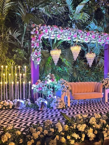A chic and modern sangeet stage with a chevron dance floor, floral arch, and unique candle-like lighting fixtures.