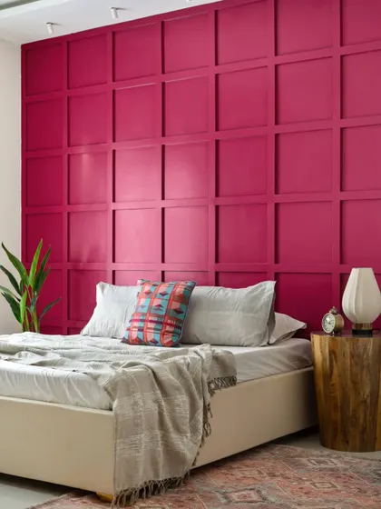 To align with Vastu, this master bedroom features a bold magenta feature wall with a simple square grid pattern. To balance the vibrant color, the rest of the room, including the bed and side table, is kept minimal and understated.