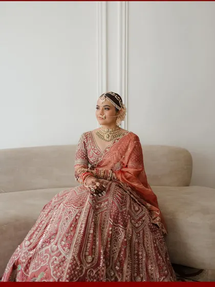 A moment of quiet elegance. This full-length portrait shows the bride seated, her beautiful lehenga spread around her, creating a look of effortless grace.