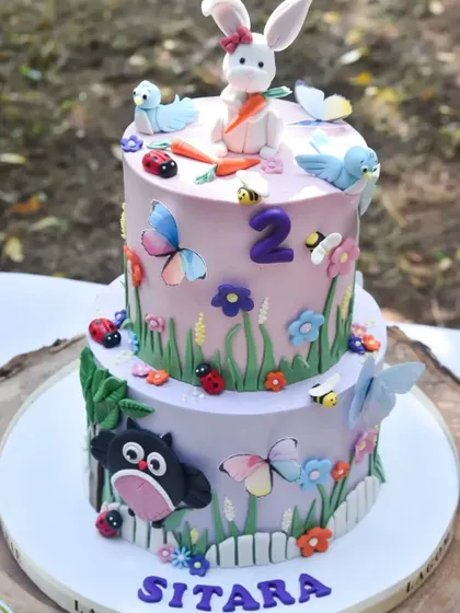 A close-up of an incredibly detailed two-tier birthday cake for a woodland-themed party. The cake features edible butterflies, bees, ladybugs, and a bunny topper, perfectly matching the event's decor.