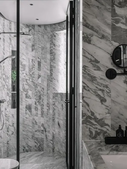 Luxury and function meet in this master bathroom, where we used vertical stripes of Statuario marble to create a curved shower wall. This technique adds a soft, sculptural feel to the space, which is unified by a sophisticated grey scale palette. The design demonstrates how we carry a home's core architectural theme through to its most private areas.
