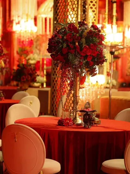 For this regal wedding, the guest tables were styled with tall, dramatic centerpieces of red roses, set against the warm glow of chandeliers and intricate gold lattice screens.
