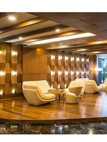 The lobby lounge of a luxury hotel in Calicut, Kerala. The design features a textured wooden wall with integrated lighting and modern, sculptural armchairs on a raised wooden platform.