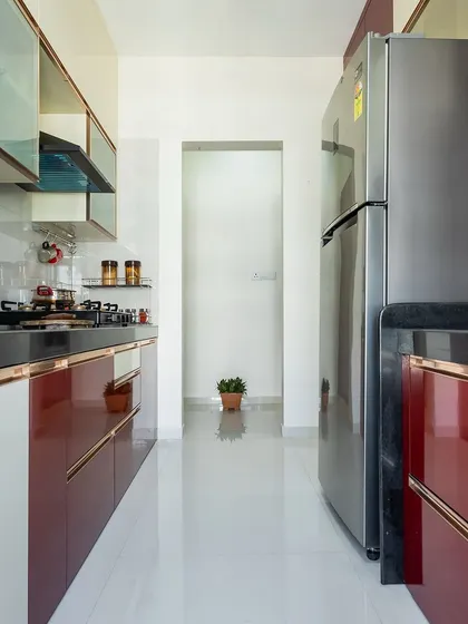 A sleek parallel kitchen in a Mumbai home, featuring glossy red cabinets with metallic trim, a black countertop, and ample storage.