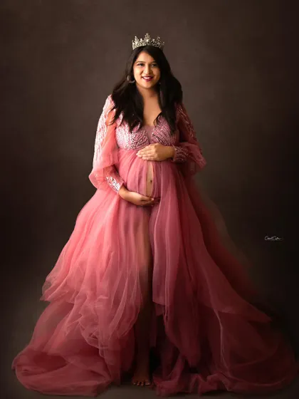 A royal portrait for a glowing queen. This mom-to-be wears a beautiful pink tulle gown, complete with a silver tiara, looking directly at the camera with a joyful smile.