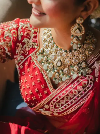 A detailed shot of the bride's exquisite jewellery and the intricate embroidery on her red blouse. We love capturing the craftsmanship and beauty of bridal attire.