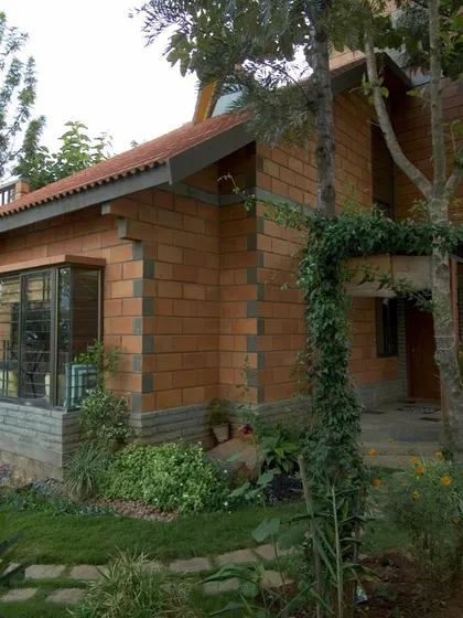 A closer look at the Sharada Residence shows how the structure is nestled among lush greenery. The use of natural brick and climbing vines helps the building merge with its garden setting over time.