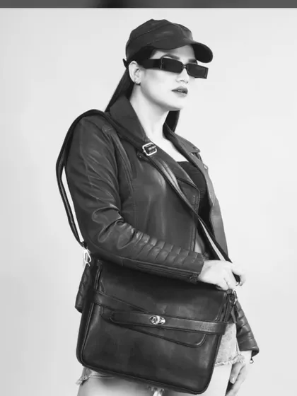 A black and white shot of a model in a leather jacket and denim shorts holding a handbag, creating an edgy, high-fashion look.