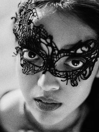 A black and white beauty editorial focused on mystery and allure. This close-up shot highlights a delicate black lace mask, drawing all the attention to the eyes.